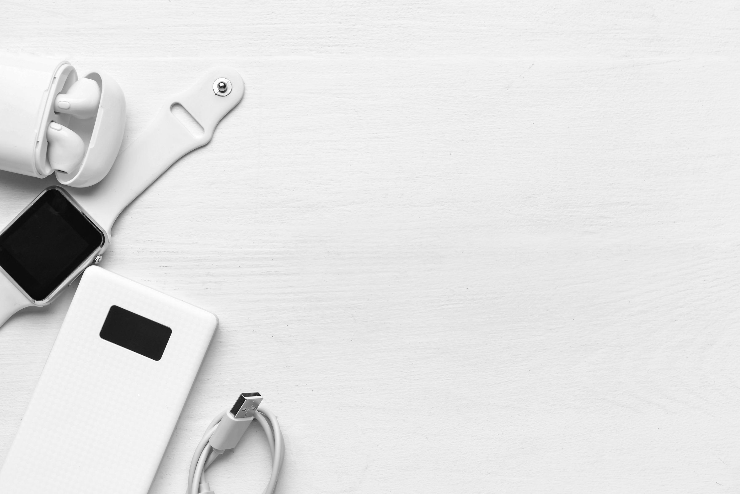 Modern Power Bank, Earphones and Smartwatch on White Wooden Background